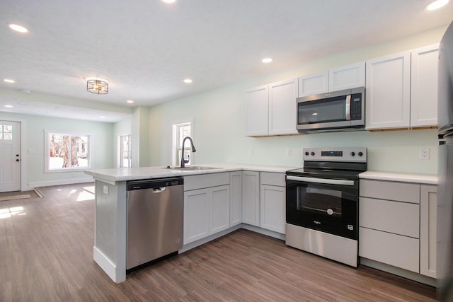 kitchen with hardwood / wood-style floors, white cabinets, stainless steel appliances, sink, and kitchen peninsula