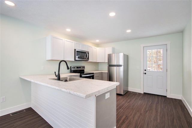 kitchen with kitchen peninsula, appliances with stainless steel finishes, sink, white cabinets, and dark wood-type flooring