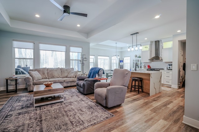 living room with sink, light hardwood / wood-style floors, a raised ceiling, and ceiling fan