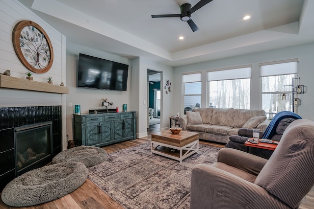 living room featuring hardwood / wood-style floors, a fireplace, a raised ceiling, and ceiling fan