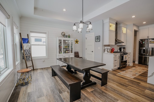 dining area featuring wood walls, wood-type flooring, a raised ceiling, and a notable chandelier