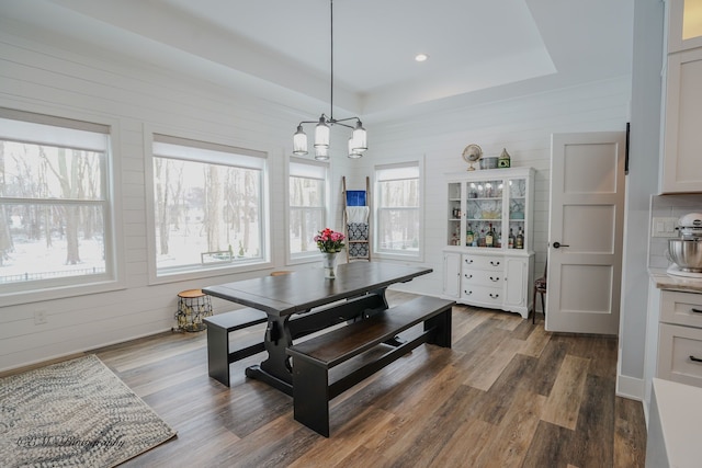 dining space with an inviting chandelier, wooden walls, dark hardwood / wood-style flooring, and a raised ceiling