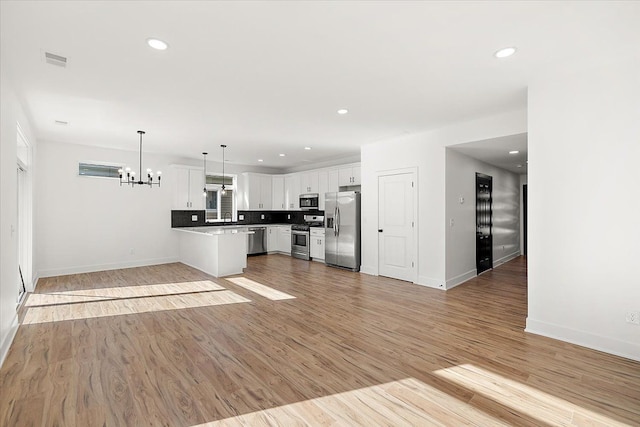 kitchen with light hardwood / wood-style floors, tasteful backsplash, hanging light fixtures, white cabinets, and stainless steel appliances