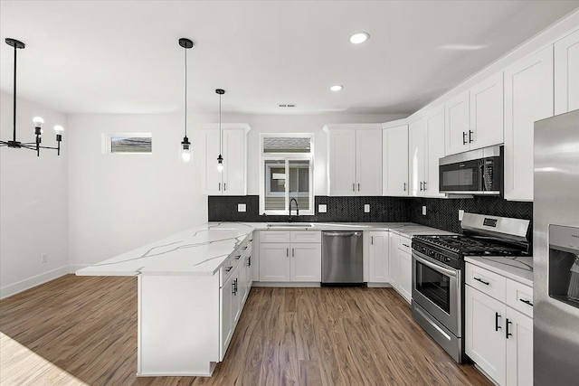 kitchen featuring light stone countertops, white cabinets, stainless steel appliances, hanging light fixtures, and kitchen peninsula