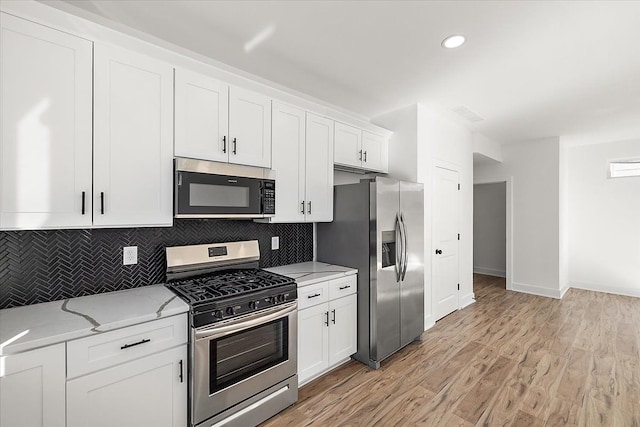 kitchen with white cabinets, stainless steel appliances, light hardwood / wood-style floors, decorative backsplash, and light stone counters