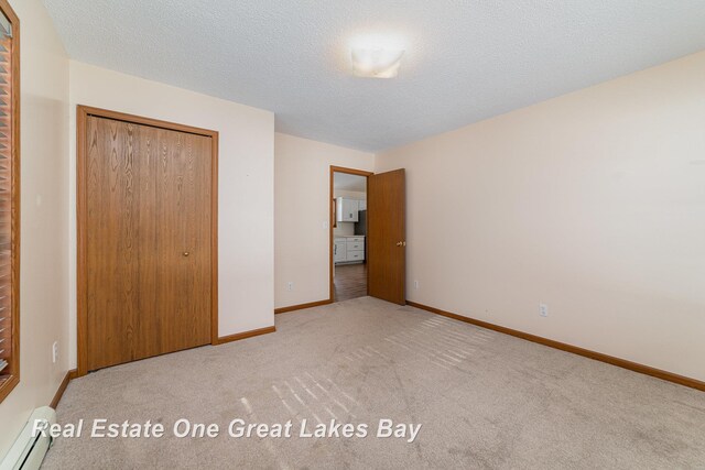 unfurnished bedroom with light carpet, a baseboard radiator, a textured ceiling, and a closet