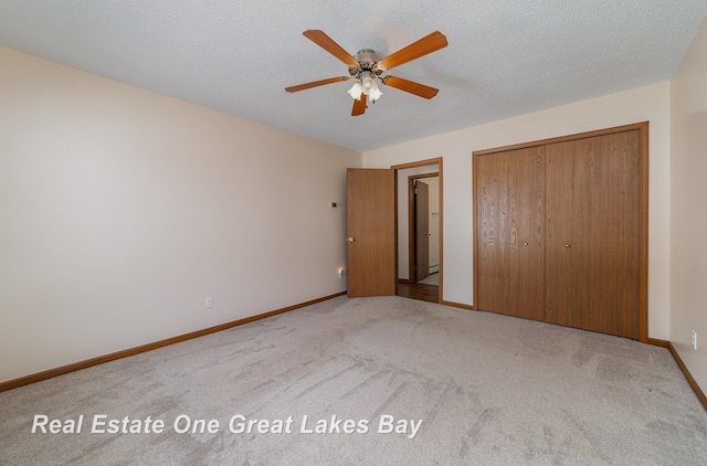 unfurnished bedroom with ceiling fan, a textured ceiling, a closet, and light carpet