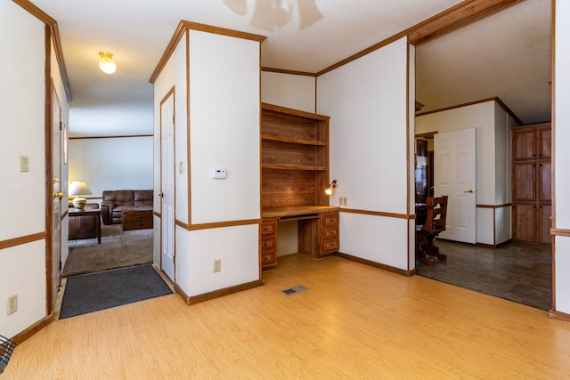 spare room with ornamental molding, built in desk, and light hardwood / wood-style floors