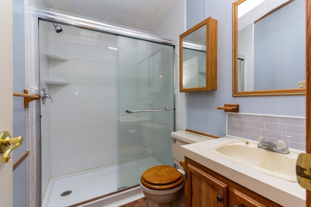 bathroom featuring vanity, toilet, a shower with door, and backsplash