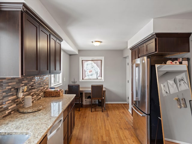 kitchen with dishwasher, decorative backsplash, dark brown cabinetry, light stone countertops, and light wood-type flooring