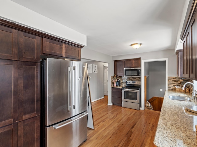 kitchen with appliances with stainless steel finishes, sink, backsplash, light stone counters, and light hardwood / wood-style floors