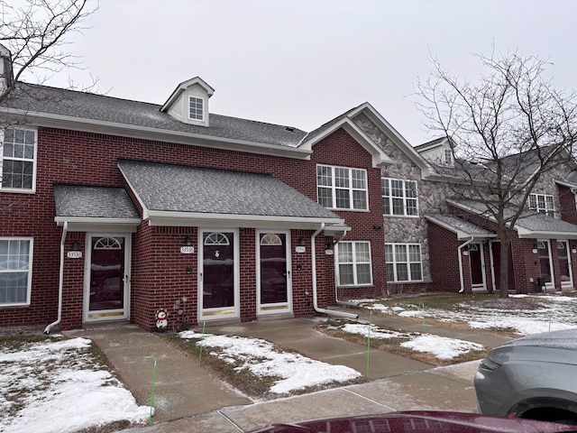 townhome / multi-family property featuring stone siding, roof with shingles, and brick siding