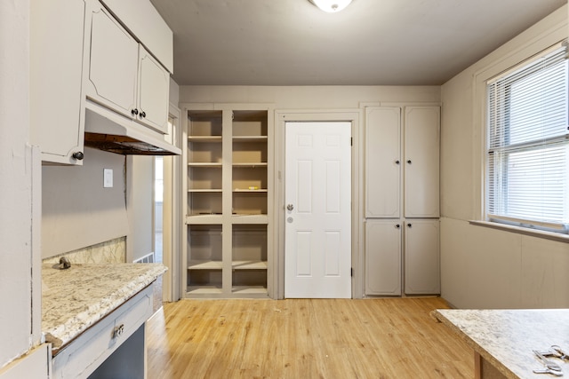 kitchen featuring white cabinets, light wood-type flooring, and light stone counters