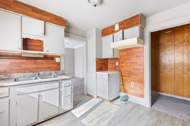 kitchen featuring white cabinets, wood walls, light hardwood / wood-style floors, and sink