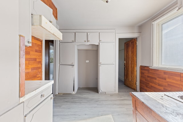 kitchen featuring white cabinetry, wooden walls, and plenty of natural light