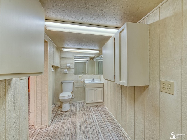 bathroom with vanity, a textured ceiling, wooden walls, and toilet