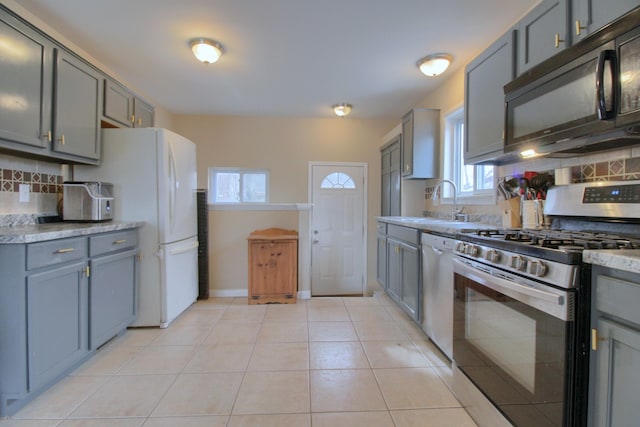 kitchen with appliances with stainless steel finishes, sink, light tile patterned flooring, gray cabinets, and decorative backsplash