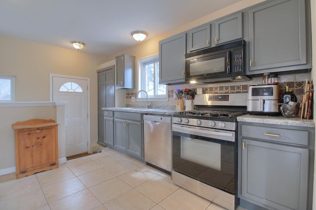 kitchen featuring appliances with stainless steel finishes, sink, backsplash, light tile patterned floors, and gray cabinets