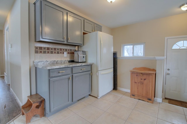 kitchen with decorative backsplash, light tile patterned floors, gray cabinetry, and white refrigerator