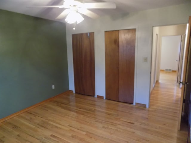 unfurnished bedroom with two closets, light hardwood / wood-style floors, and ceiling fan