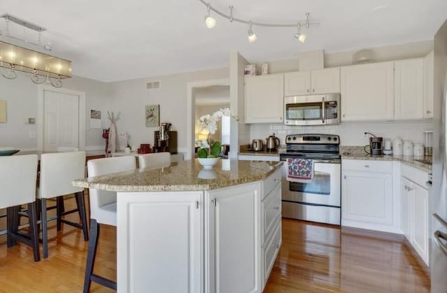 kitchen with white cabinets, a kitchen island, stainless steel appliances, a kitchen breakfast bar, and light hardwood / wood-style flooring