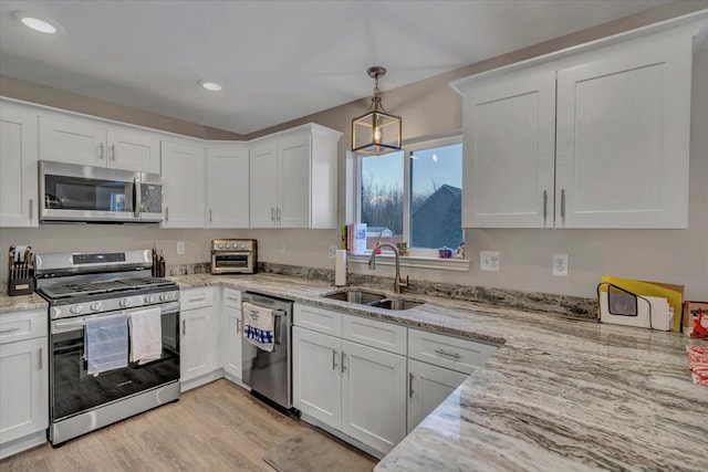 kitchen featuring light hardwood / wood-style floors, appliances with stainless steel finishes, white cabinetry, sink, and pendant lighting