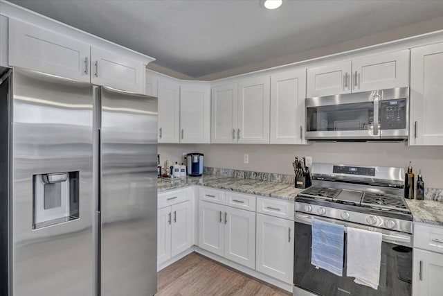 kitchen featuring light stone counters, white cabinetry, appliances with stainless steel finishes, and light hardwood / wood-style flooring