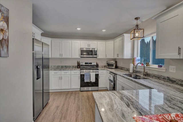 kitchen featuring pendant lighting, appliances with stainless steel finishes, sink, white cabinetry, and light stone counters