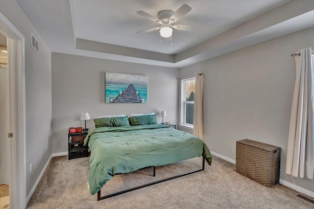 carpeted bedroom with ceiling fan and a tray ceiling