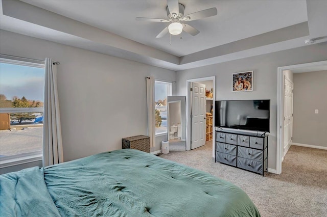 bedroom with ceiling fan, multiple windows, light colored carpet, and a tray ceiling