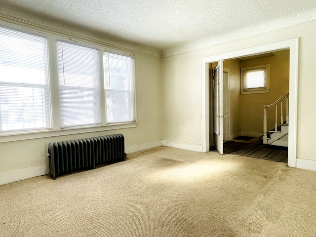 empty room featuring radiator heating unit, light colored carpet, and a textured ceiling