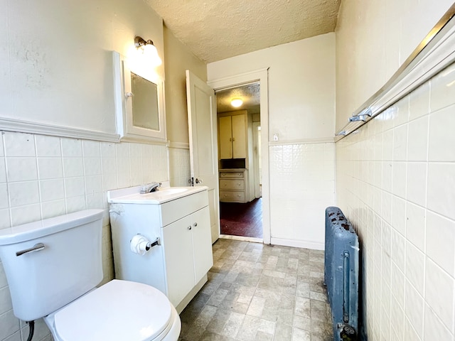 bathroom with radiator, tile walls, vanity, toilet, and a textured ceiling