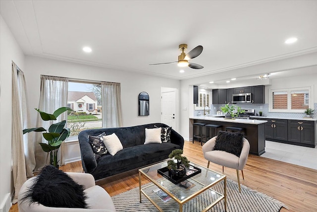 living room with ceiling fan, plenty of natural light, sink, and light wood-type flooring