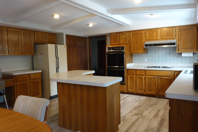 kitchen with a kitchen island, double oven, ventilation hood, white fridge, and gas cooktop