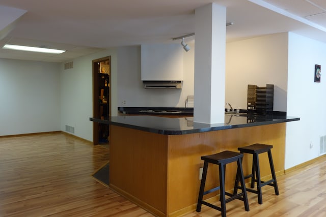 kitchen with a breakfast bar area, white cabinetry, track lighting, light hardwood / wood-style floors, and kitchen peninsula