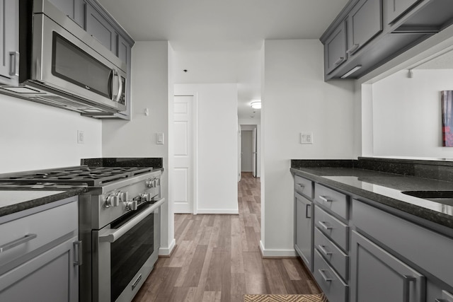 kitchen featuring dark wood-type flooring, sink, dark stone countertops, appliances with stainless steel finishes, and gray cabinets