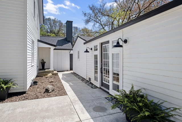 101 Carl Dr NE, Ada, MI 49301 - view of exterior entry featuring a patio area, roof with shingles, and a chimney