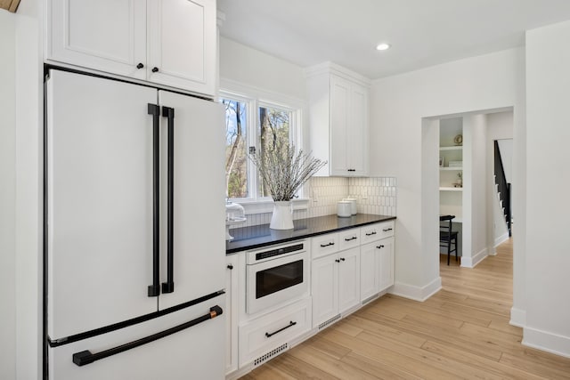 101 Carl Dr NE, Ada, MI 49301 - kitchen with white appliances, dark countertops, tasteful backsplash, white cabinetry, and light wood-style floors