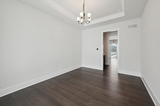 spare room featuring a raised ceiling, dark hardwood / wood-style floors, and an inviting chandelier