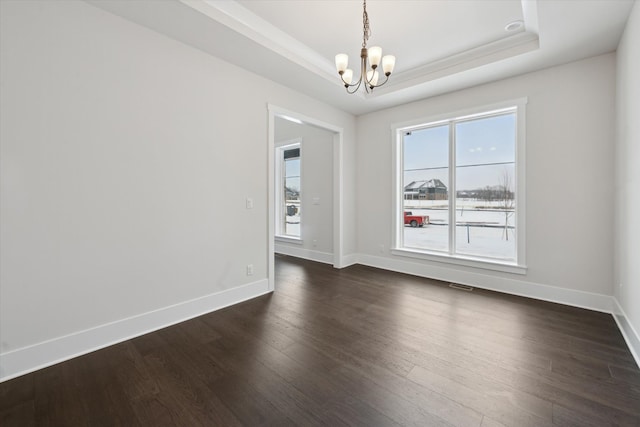 empty room with dark wood-type flooring, a notable chandelier, and a tray ceiling