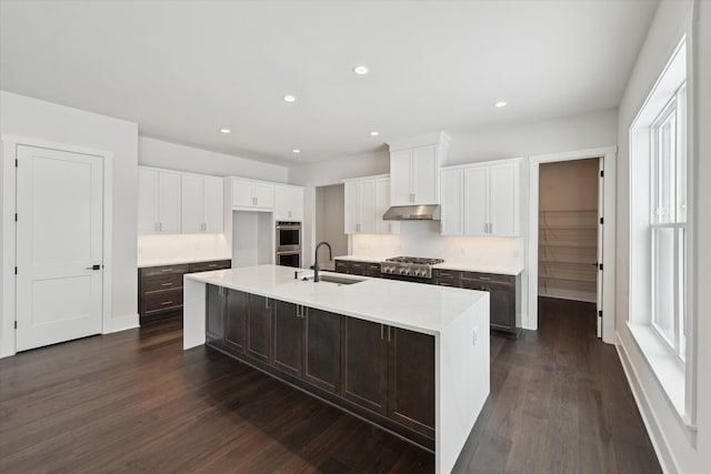 kitchen with sink, white cabinets, a kitchen island with sink, stainless steel appliances, and dark wood-type flooring