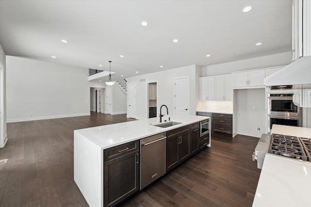 kitchen featuring sink, appliances with stainless steel finishes, dark hardwood / wood-style floors, pendant lighting, and a kitchen island with sink