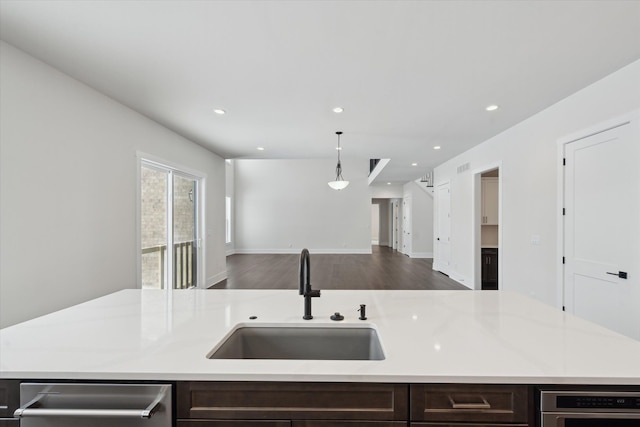 kitchen featuring dark brown cabinetry, sink, decorative light fixtures, light stone countertops, and a kitchen island with sink