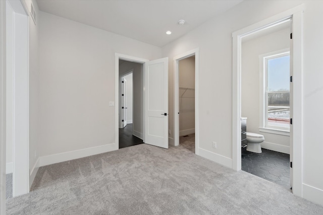 unfurnished bedroom featuring a spacious closet, light colored carpet, a closet, and ensuite bathroom