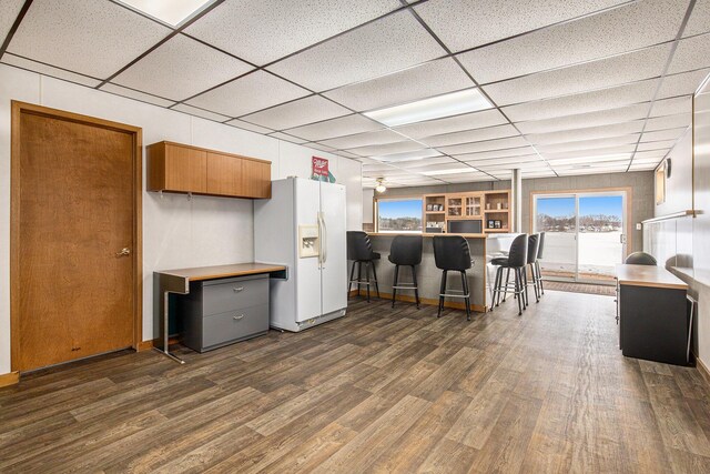 kitchen featuring a breakfast bar area, dark hardwood / wood-style floors, white fridge with ice dispenser, a drop ceiling, and kitchen peninsula