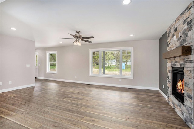 unfurnished living room featuring a stone fireplace, hardwood / wood-style floors, and ceiling fan