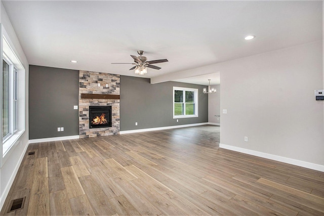 unfurnished living room featuring hardwood / wood-style floors, ceiling fan with notable chandelier, and a fireplace