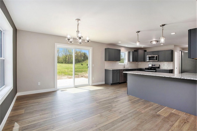 kitchen featuring hanging light fixtures, stainless steel appliances, light stone countertops, light hardwood / wood-style floors, and decorative backsplash