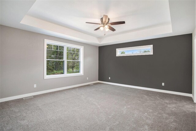 empty room with a raised ceiling, ceiling fan, and carpet