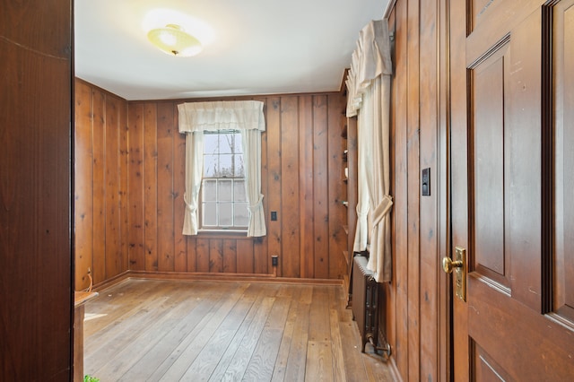 spare room featuring radiator, light hardwood / wood-style floors, and wood walls